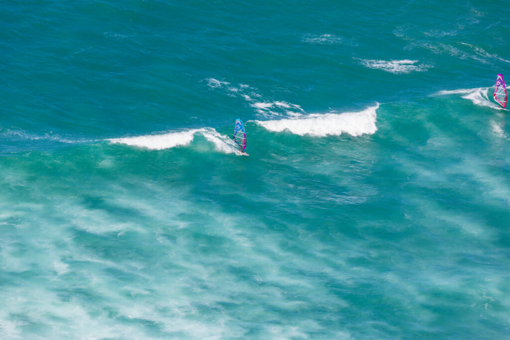 Two windsurfers riding waves in a turquoise ocean