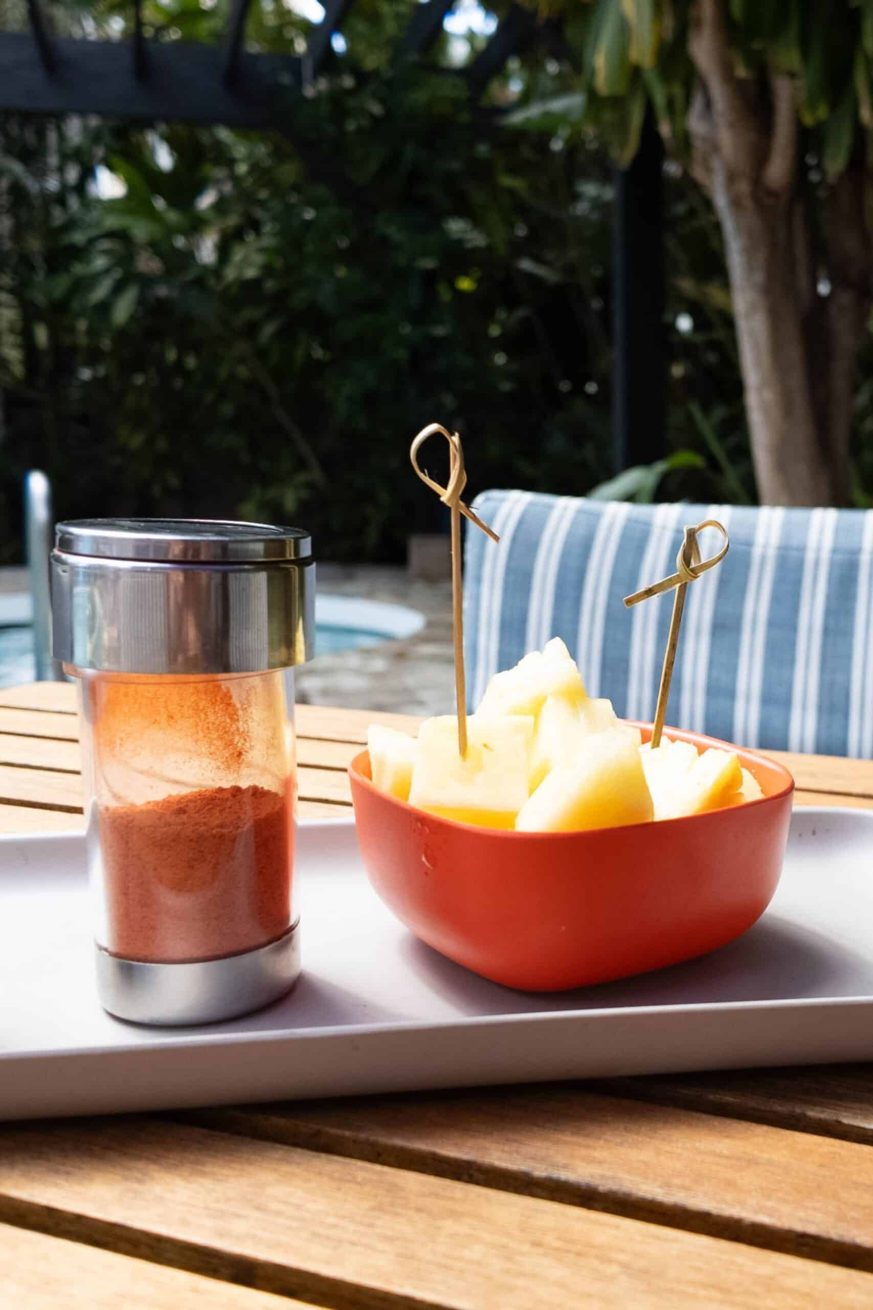 A plate of pineapple and spices on a table in front of a pool