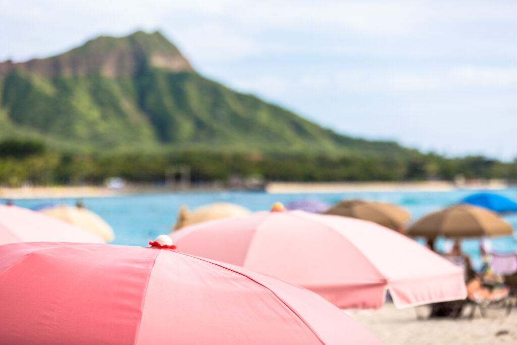 Pink beach umbrellas with the ocean and an island mountain in the background