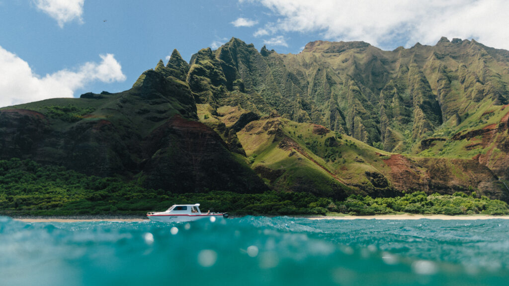 A white boat in the water in front of the tall Na Pali Coastline