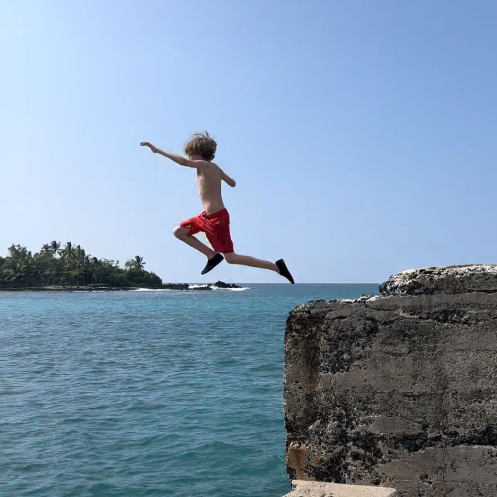 A boy with red shorts jumping off a cliff into water