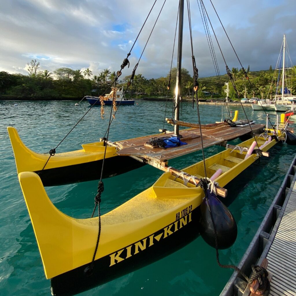 A yellow traditional Hawaiian canoe with a beautiful tropical bay behind it
