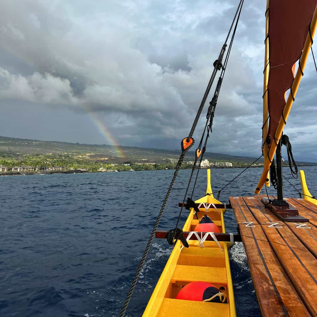 A yellow traditional Hawaiian canoe with a rainbow in the background