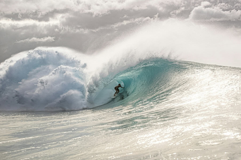A surfer standing up on his board in a huge wave