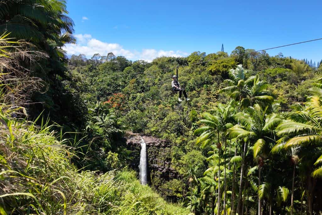 A boy ziplining over a waterfall and tropical plants