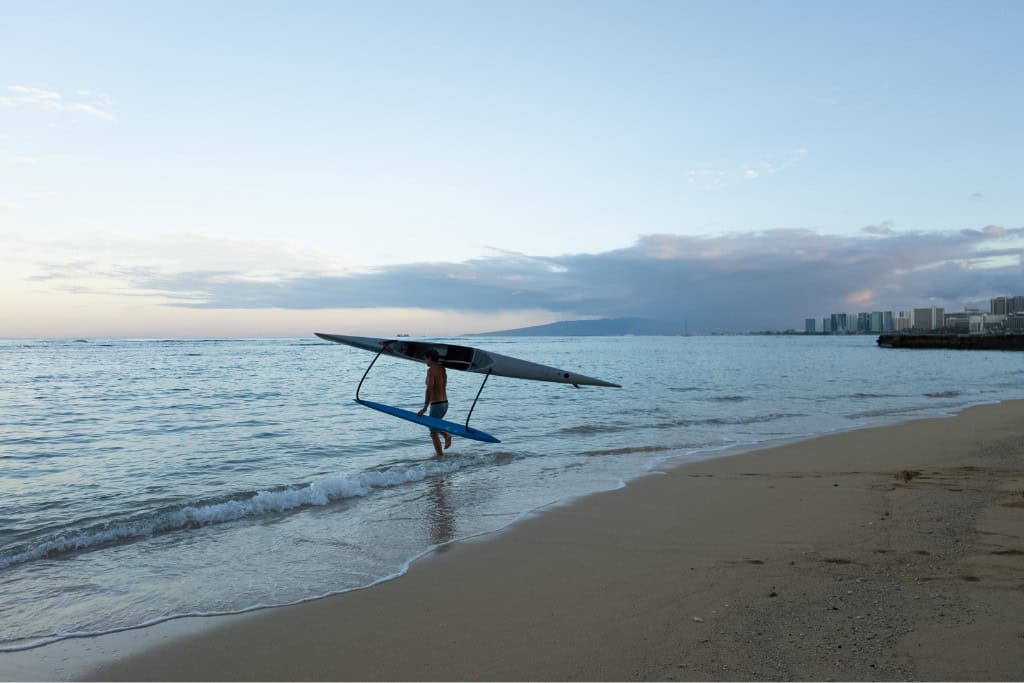 A man carrying a kayak into the water in the morning with Waikiki in the background