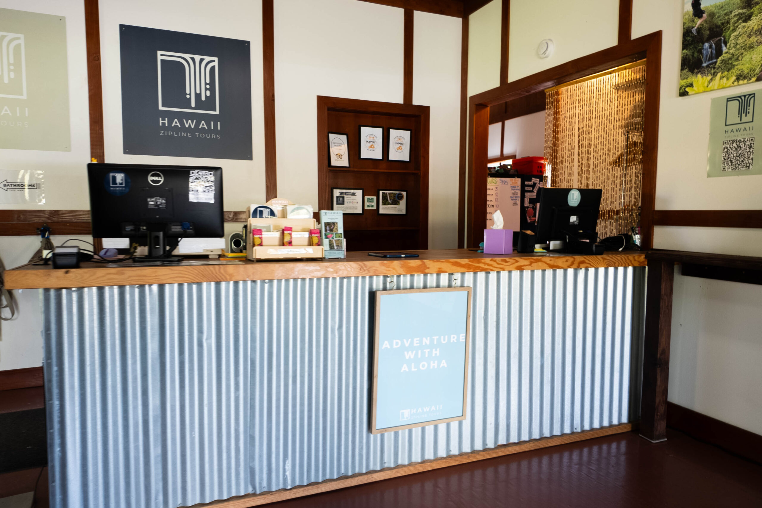 A reception desk with a sign behind it that says Hawaii Zipline Tours and a sign in front of it that says Adventure With Aloha