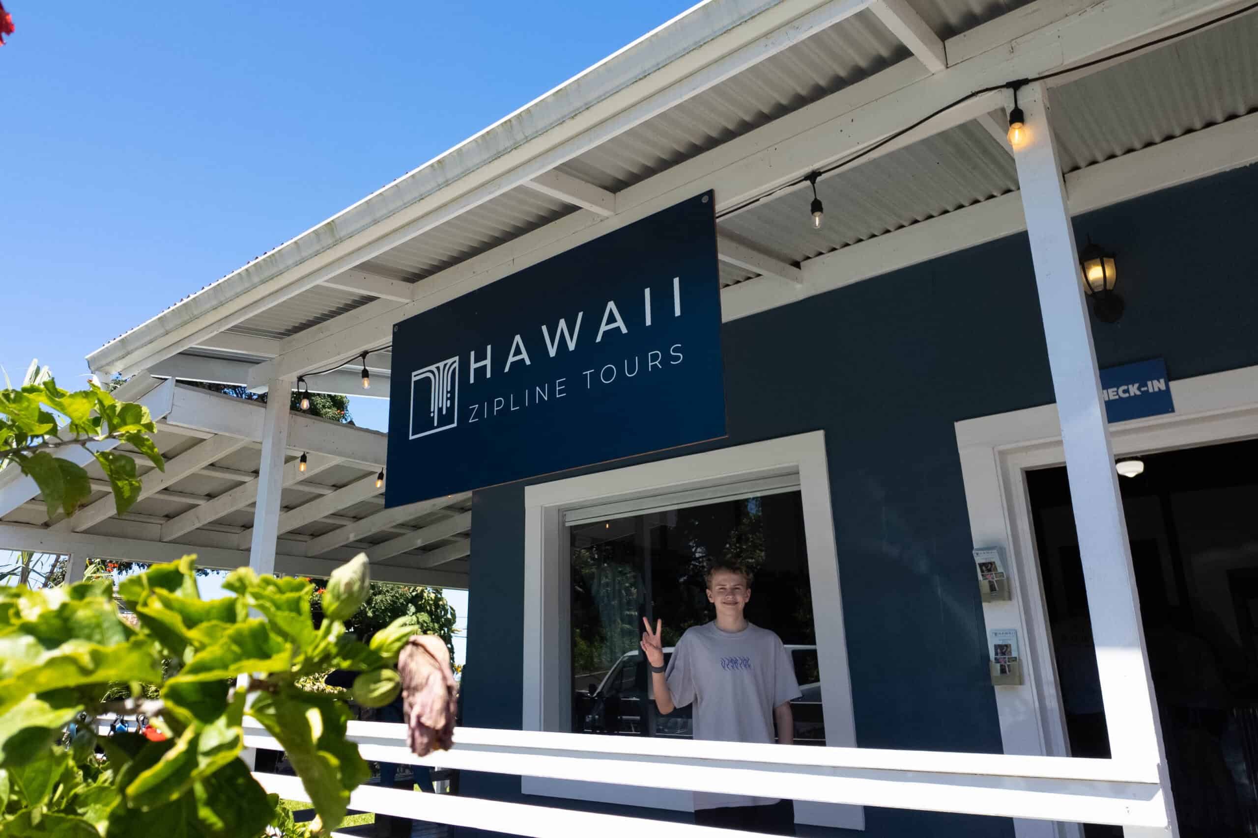 A boy waving under a sign that says Hawaii Zipline Tours