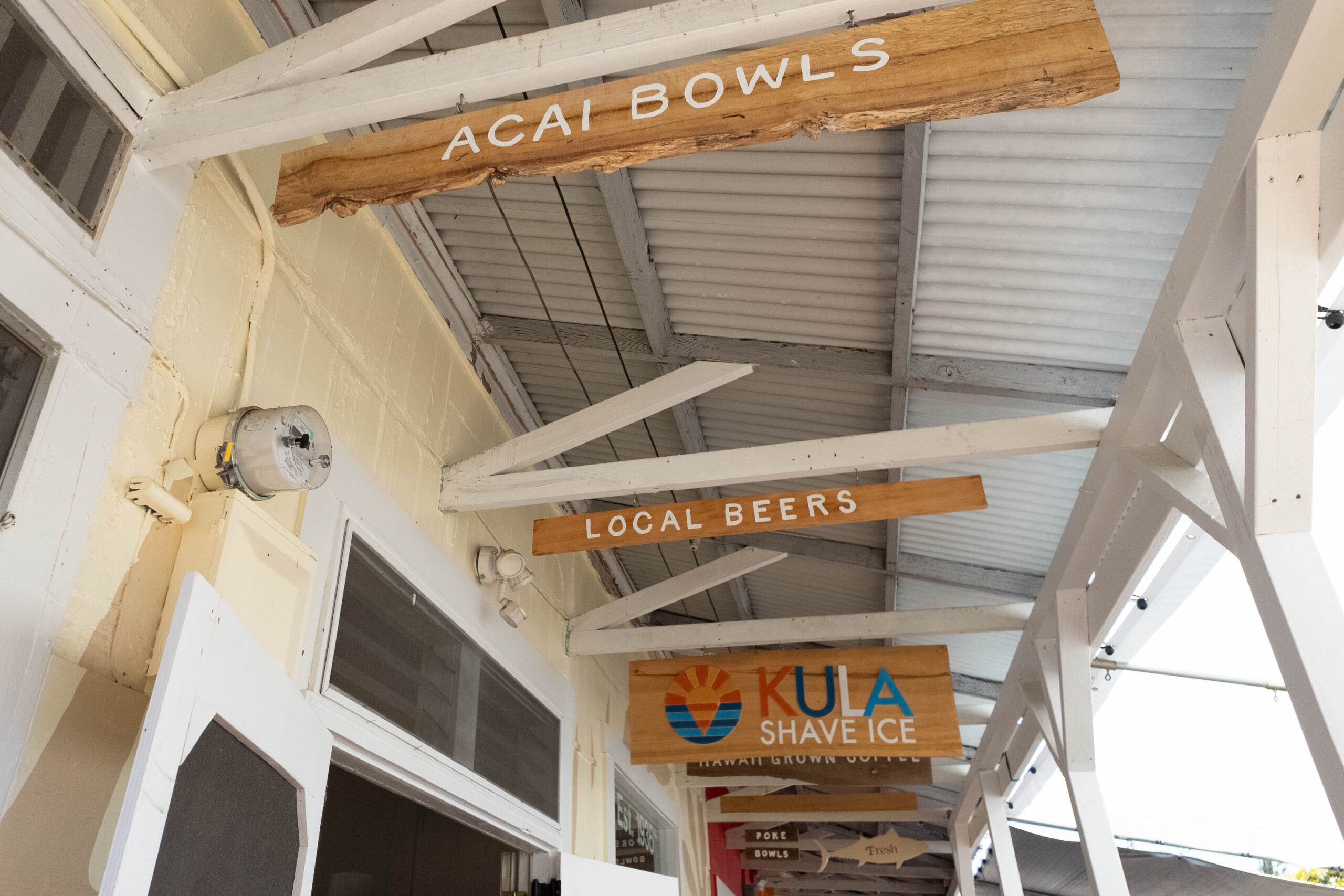 A white ceiling with signs that say Acai Bowls, local beers anad Kula Shave Ice