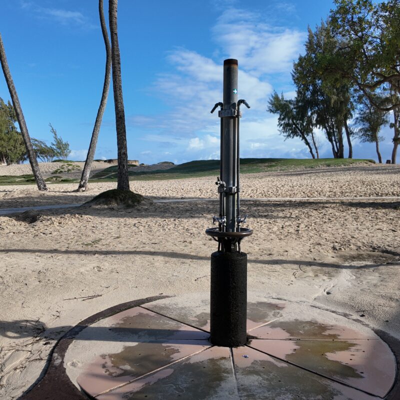 A beach shower surrounded by sand and tropical trees