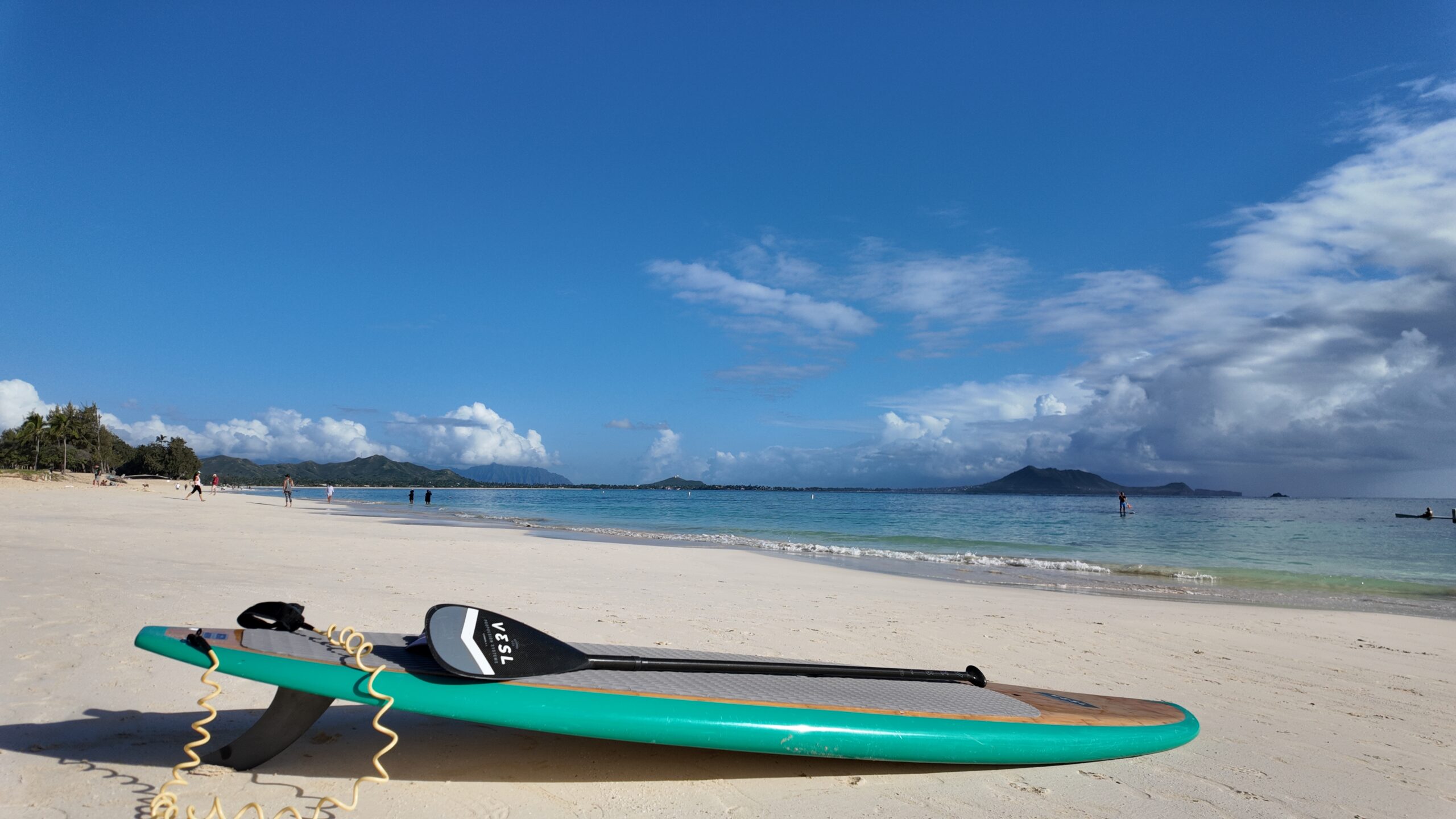 A paddleboard sitting on a white sand beach with the ocean behind it.