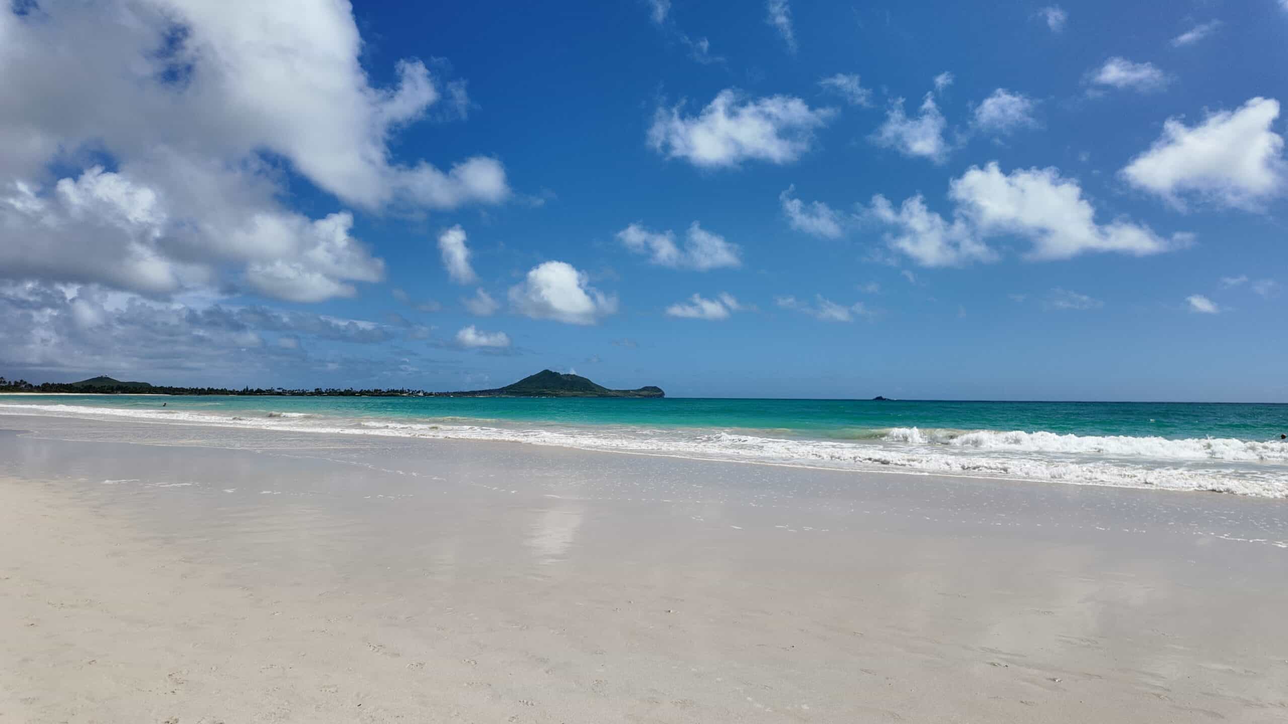 A white sand beach with turquoise water and mountains in the background on a clear day.