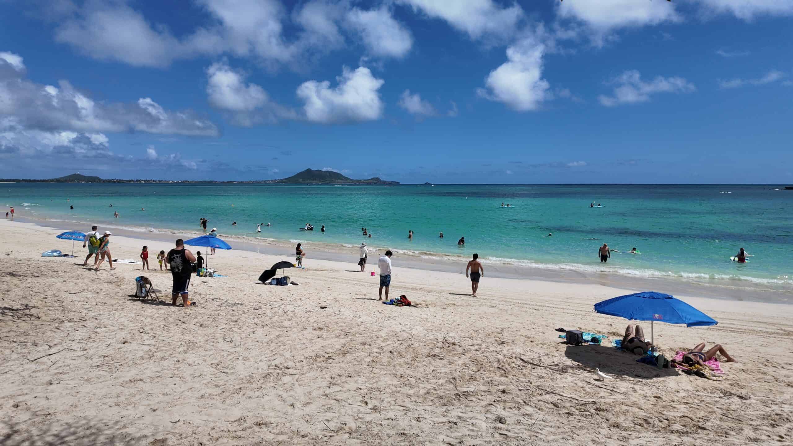 Beach-goers on a white sand tropical beach with umbrellas and turquoise waters.