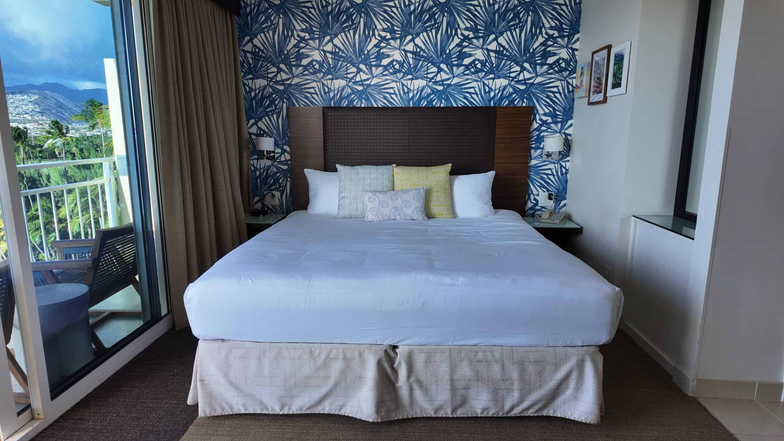 A hotel bed with tropical wallpaper and pillows, Honolulu out the window in the background