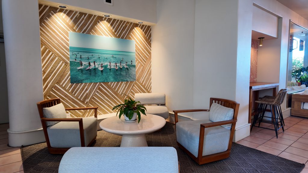 A seating area in a tropical hotel with a photograph of a surfers at Waikiki in the background.