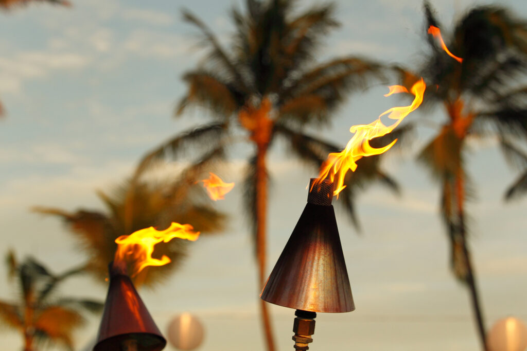 Tiki torches lit up in front of palm trees