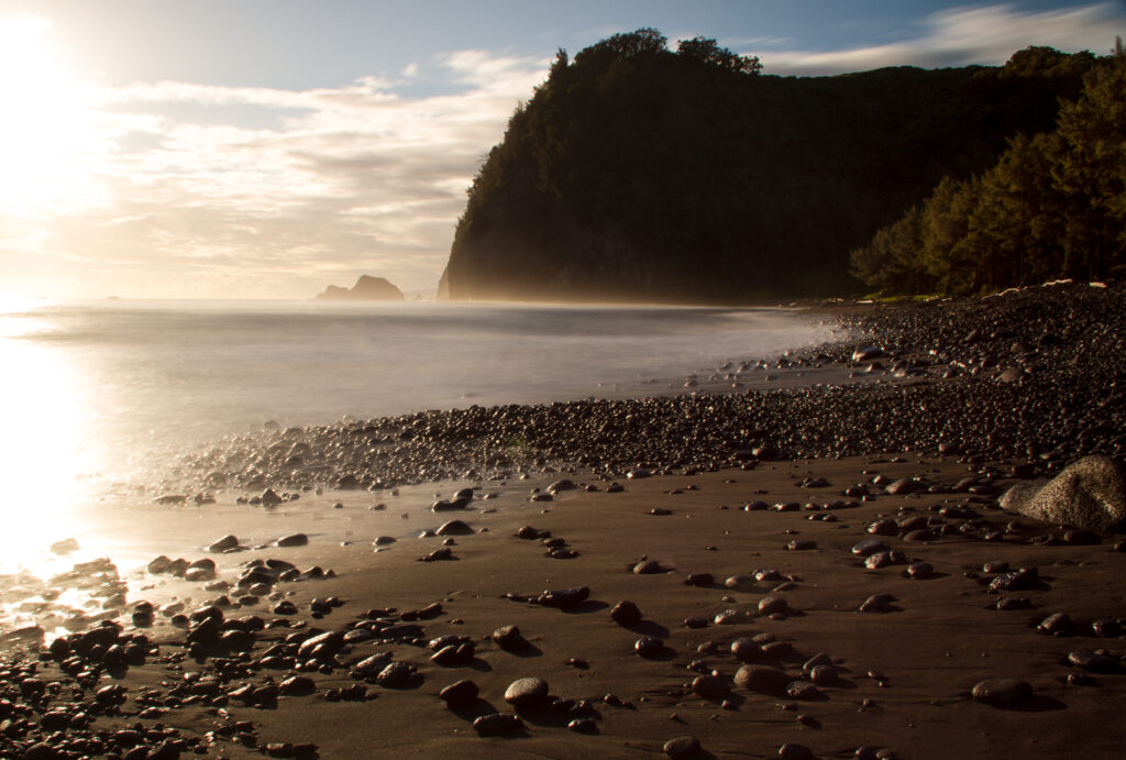 A moody black sand beach with rocks in the sand and a mountain in the background