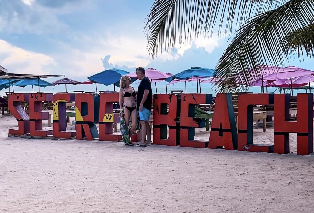 husband-and-wife-in-front-of-secret-beach-sign-ambergris-caye-belize