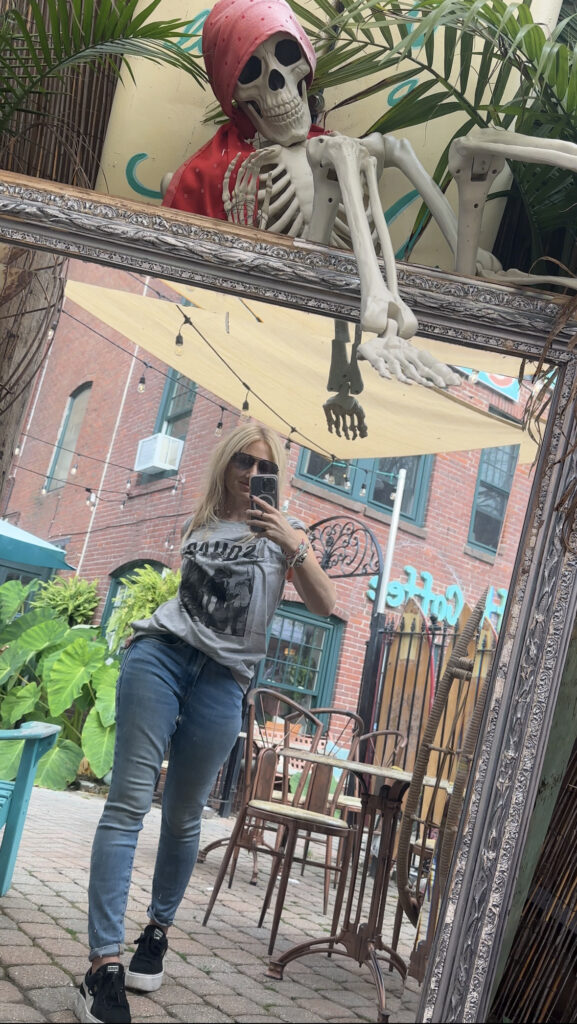 blonde-woman-in-gray-hocus-pocus-shirt-standing-in-front-of-mirror-taking-selfie-at-castaways-gloucester