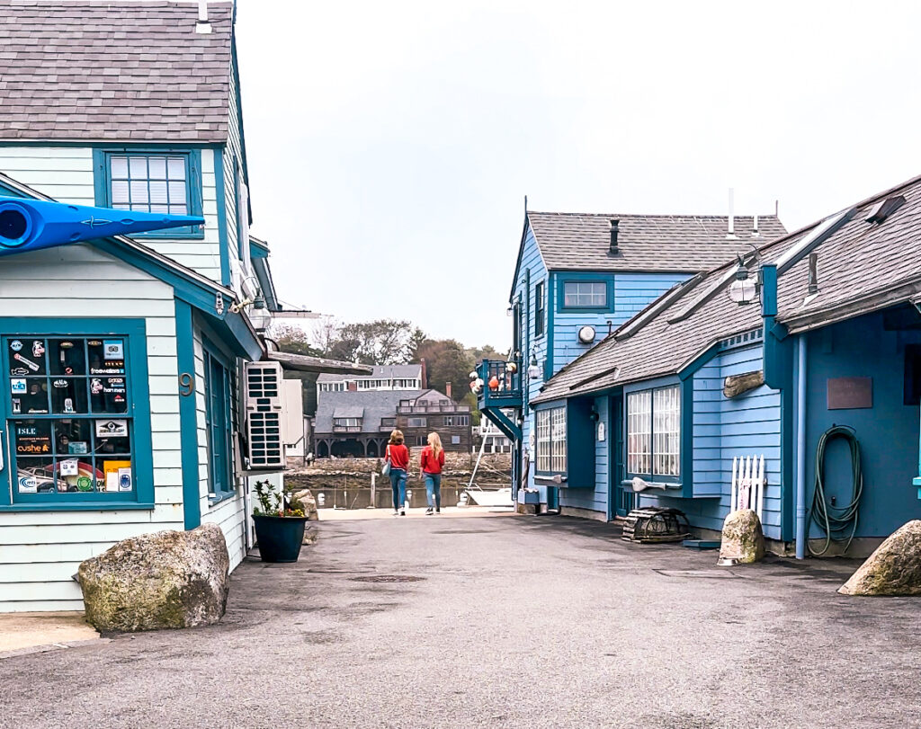 women-in-orange-sweaters-looking-at-water-in-rockport-surrounded-by-blue-buildings