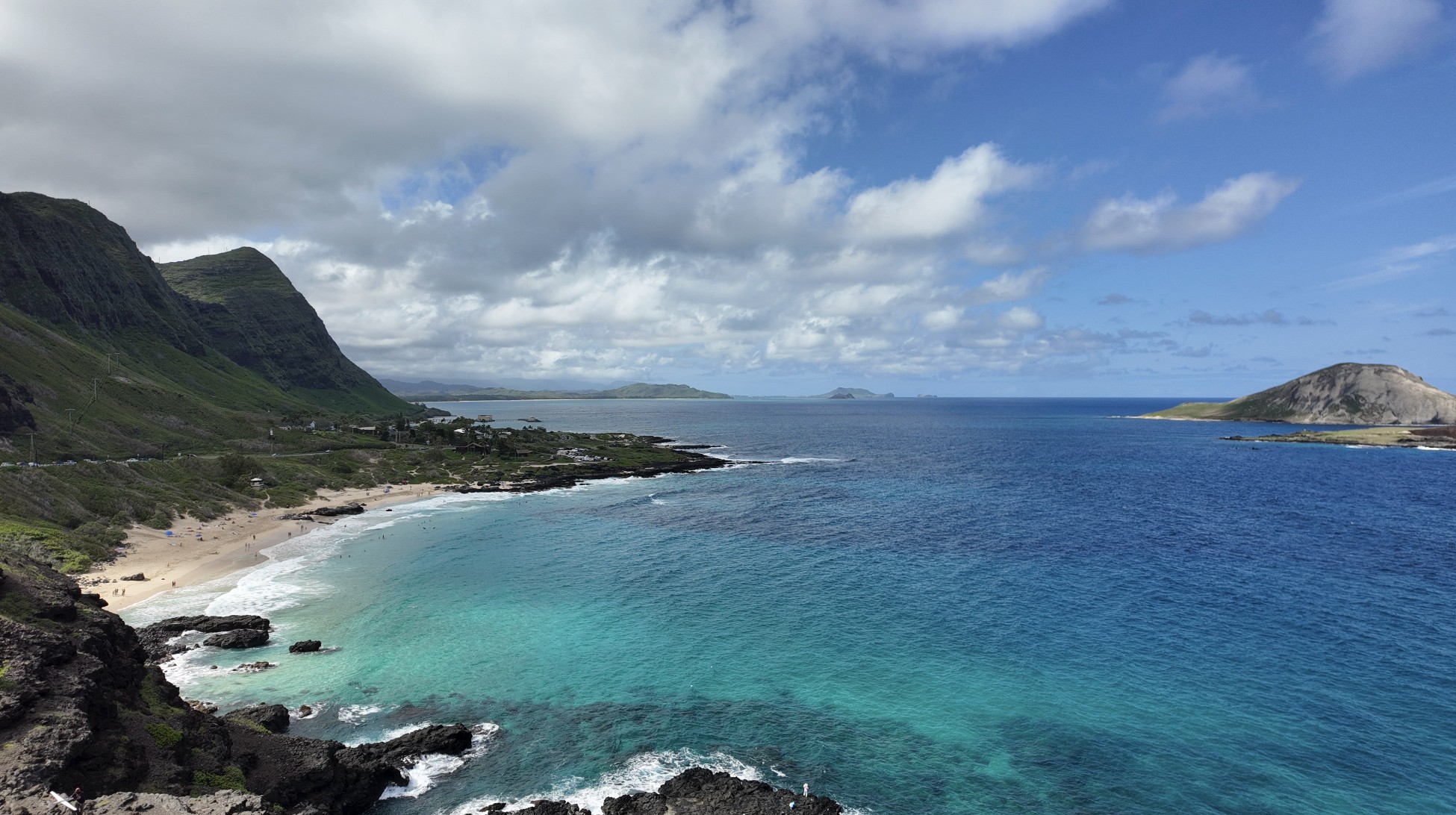 An aerial view of an island with a beach and a turquoise ocean with an island in the distance