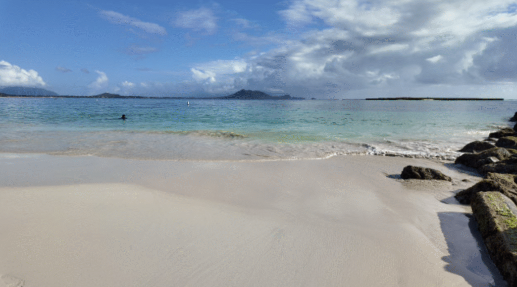 A beautiful white sand beach with mountains in the distance and a boat ramp to the right